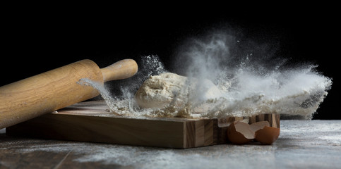 Studio photo of a ball of bread dough falling on flour with roller - 234529182
