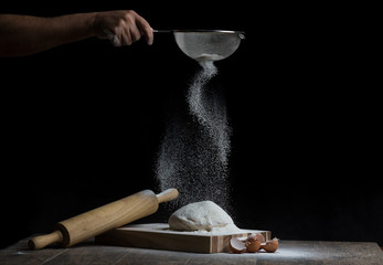 Flour is sprinkled over a ball of dough on a wooden board with roller