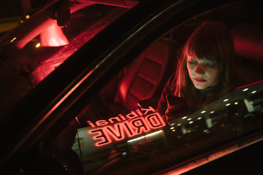 Young woman in car with smartphone and reflection of Kibiniai drive inscription