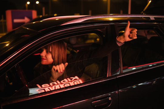 Young woman in car with thumb up and reflection of Kibiniai drive inscription