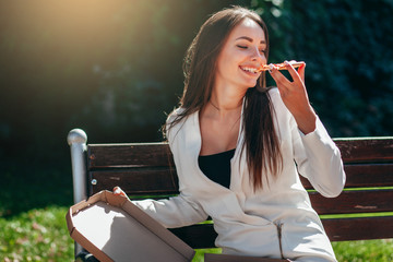 Smiling business girl in white dress eating pizza in street 