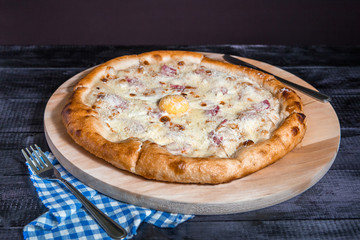 Pizza Carbonara with egg and ham on dark wood background
