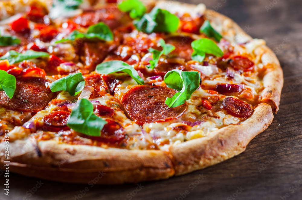 Wall mural sliced Pepperoni Pizza with Mozzarella cheese, salami, chorizo, tomato sauce, pepper, Spices and Fresh arugula. Italian pizza on wooden table background