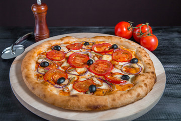 Rustic pizza with salami, mozzarella, fresh tomatoes, red onion, black olives and fresh basil. Home made pizza.