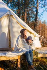 Young mother sitting with her kid near traditional canvas bell tent