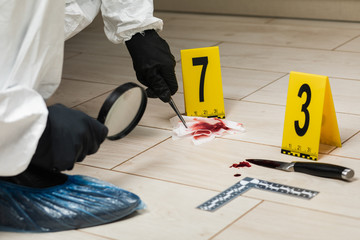 A criminology expert looks through a magnifying glass at a bloody napkin at the crime scene