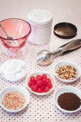 A variety of ice cream toppings including cream, cherries, nuts and sprinkles. 