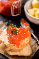 Salmon red caviarin a glass jar and Sandwiches with butter and parsley on slate cutting board on a light marble background. Seafood. Healthy Food Concept. Snack.