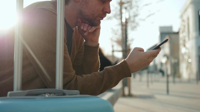 man sitting at the airport using mobile phone on bench near luggage baggage waiting flight airport terminal or train station bus stop