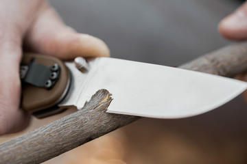 Close-up of the tourist's hands, sharpening a stick with a knife. The concept of travel, extreme...