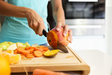 Hands of a woman cutting some vegetables and fruits in wooden table in the kitchen.