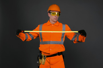 Fototapeta premium Shocked builder measurer with meter roulette in the hands surprised by the size isolated on gray background.