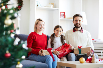 Obraz na płótnie Canvas Happy young casual family with giftboxes looking at you while enjoying xmas eve at home