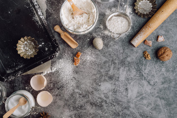 Healthy baking ingredients. Spoon with flour, dishes, eggs, butter salt and rolling pin on a grey background.Bakery background frame. Top view, copy space.