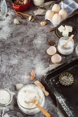 Healthy baking ingredients. Spoon with flour, dishes, eggs, butter salt and rolling pin on a grey background.Bakery background frame. Top view, copy space.