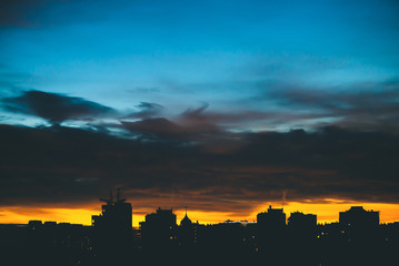 Cityscape with wonderful varicolored vivid dawn. Amazing dramatic blue cloudy sky above dark silhouettes of city buildings. Atmospheric background of orange sunrise in overcast weather. Copy space.