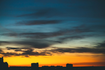 Cityscape with wonderful varicolored vivid dawn. Amazing dramatic blue cloudy sky above dark...