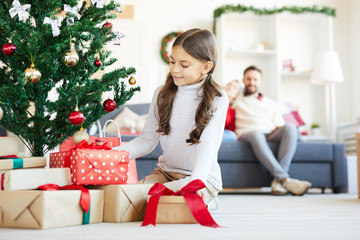 Little girl putting giftboxes for guests under decorated Christmas tree at home