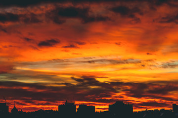 Cityscape with vivid fiery dawn. Amazing warm dramatic cloudy sky above dark silhouettes of city...
