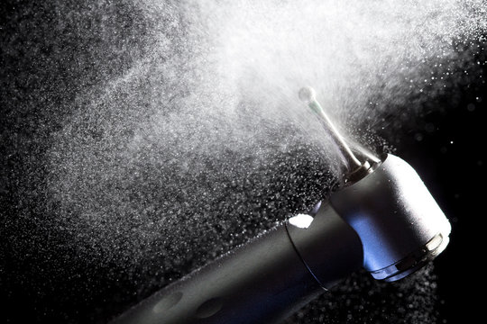 Dental handpiece with diamond bur and water splash motion on dark background.