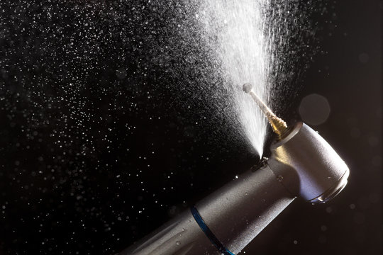Dental handpiece with diamond bur and water splash motion on dark background.