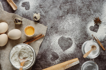 Fototapeta na wymiar Healthy baking ingredients. Background with flour, rolling pin, eggs, and heart shape on kitchen gray kitchen table. Top view for Valentines day cooking. Copy space.