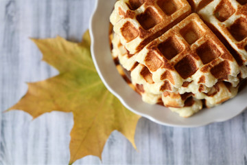 Belgian waffles and yellow maple leaf on light wooden table. Freshly cooked homemade dessert, tasty breakfast