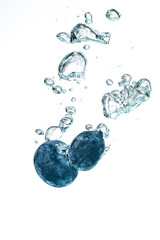 Two blueberry’s splashing into crystal clear water with air bubbles