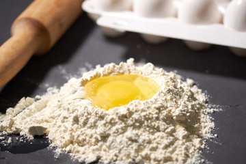 broken egg in flour, next to a rolling pin and whole eggs, selective focus