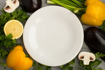 Empty white  plate, vegetables and fruit on the grey wooden background.Healthy food ingredients.Top view.Copy space.