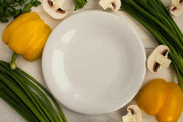 Empty white  plate and vegetables on the wooden background.Healthy food ingredients.Top view.Copy space.