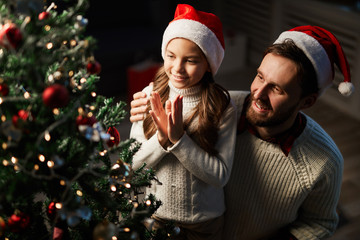 Cute little girl admiring Christmas tree after decorating it with father