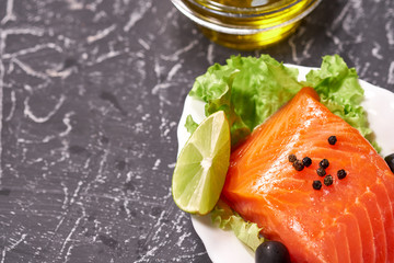 A piece of salmon on a white plate with olives and lemon, on a gray background. Selective focus. space for text.