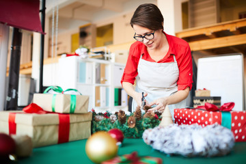 Designer of gifts and decorations making coniferous xmas wreath with pine cones and bows