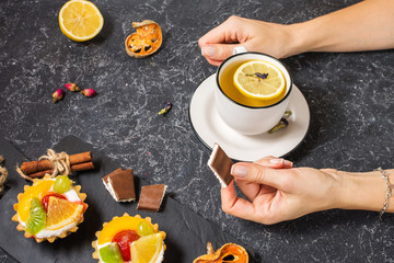 Female hands hold cup of tea on black stone background.