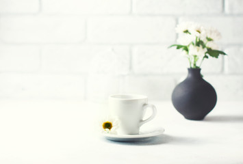 A cup of hot coffee and a bouquet of camomiles in a vase.