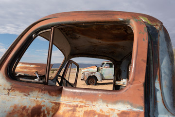 Close up of old antique rusty truck door with second rusty vintage truck in distant with overcast...
