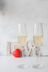 two festive glasses with champagne on a white background with a red heart