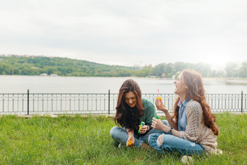 Two sisters having fun while making bubbles and sitting on the g