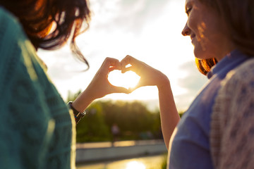 Two girls are showing heart from hands at sunset