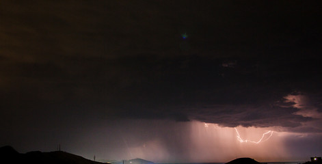 a black stormy sky lit by lightning under hills