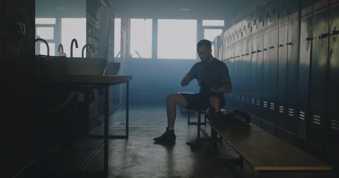 MS DOLLY IN Caucasian male wraps his hands in locker room before boxing martial arts training. 4K UHD 60 FPS SLOW MOTION