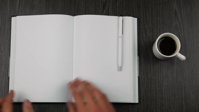 Espresso cup and diary on dark wooden table. Businessman's hand opens the diary.