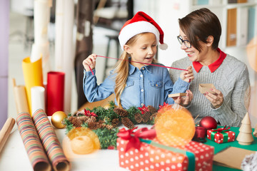 Cheerful little girl in xmas cap and her mother discussing what to put into small giftbox