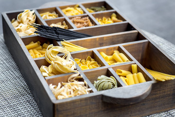 a wooden box with cells in which traditional Italian pasta is poured, raw products ready for cooking are on the table.