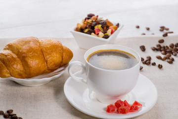 cup of coffee and a croissant on a served table with flower buds