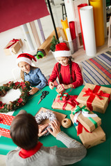 Cute girls and their mom sitting by table in front of each other and making gifts