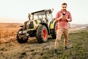 Farmer working and harvesting using smartphone in modern agriculture - tractor background
