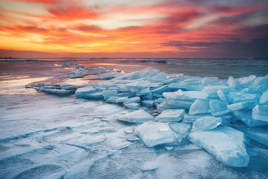 Winter landscape on seashore during sunset. Lofoten islands, Norway. Ice and sunset sky. Natural winter landscape