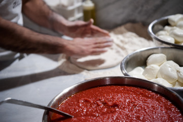 Preparing Pizza dought on a marble countertops. Tomato sauce and mozzarella in the foregound.